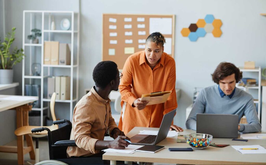 A team of marketing professionals, including a Black man in a wheelchair, a Black woman, and a white man, are having a discussion at a table.