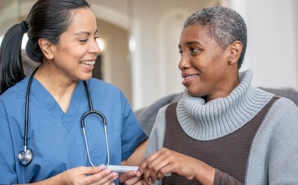A nurse and person living with diabetes are facing eachother and smiling as the nurse hands the person with diabetes a medication injection pen.